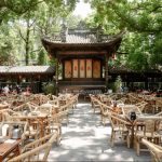 Traditional outdoor teahouse at Tiexiangsi Water Street in Chengdu, featuring bamboo chairs, tea tables, and a classical Sichuan-style stage surrounded by lush green trees.
