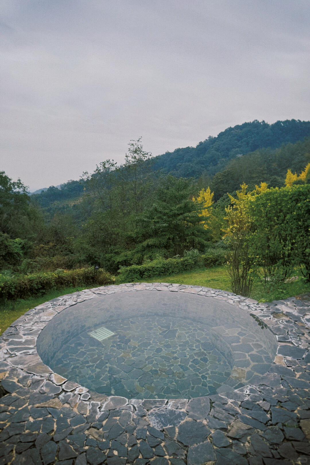 Outdoor stone hot tub set in an open grassy area with surrounding mountain views.